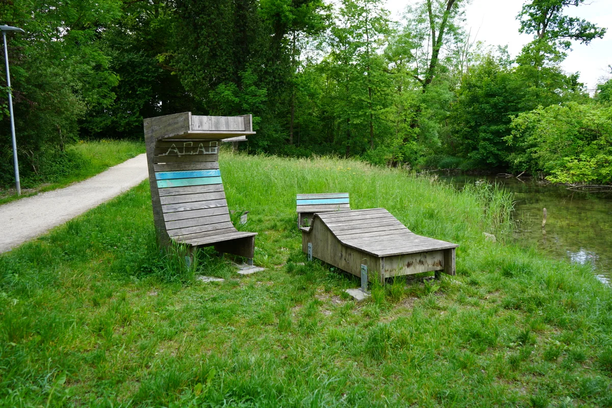 Zwei Holzkonstruktionen als Liegestuhl auf einer Wiese am Fluss.